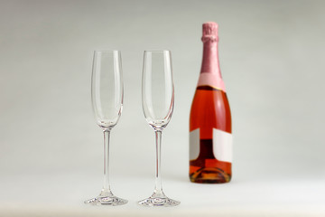 Two crystal copes with a bottle of champagne rose in a white background.