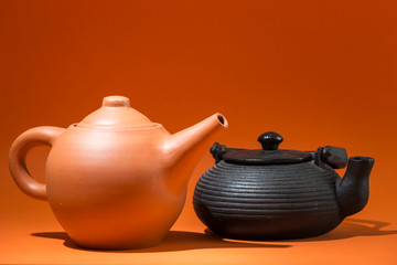 two very different teapots on an orange background