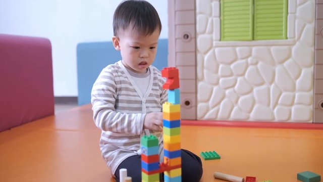 Cute little Asian 2 - 3 years old toddler boy child having fun playing with colorful plastic blocks indoor at play school / nursery / living room, Educational toys for young children concept