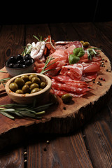 Marble cutting board with prosciutto, bacon, salami and sausages on wooden background. Meat platter