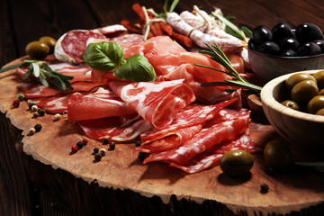 Marble cutting board with prosciutto, bacon, salami and sausages on wooden background. Meat platter