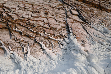 Scenic ribbed rock wall covered with snow and ice, perspective view from the bottom, winter mountain background or texture