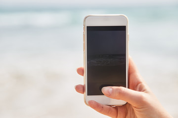 Mobile phone in female hand on the background of the beach and ocean