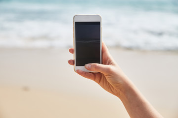 Mobile phone in female hand on the background of the beach and ocean