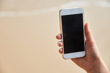 Mobile phone in female hand on the background of the beach and ocean