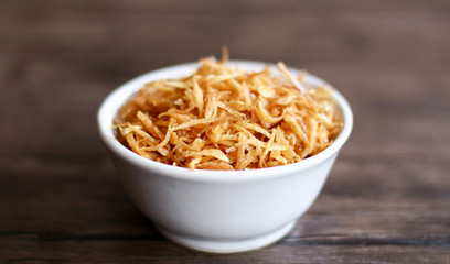 Fried red onion on wood background. Can used as topping on the side with the chicken, meat or fish dishes.