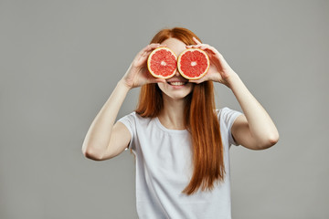 fubby red-haired girl with grapefruit on her eyes. close up photo. fun, entertainment . isolated...
