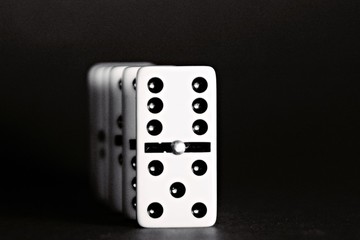 Bright dominoes against a black background with shallow depth of field as a concept for business concepts and subsequent reactions of individual decisions and individual actions
