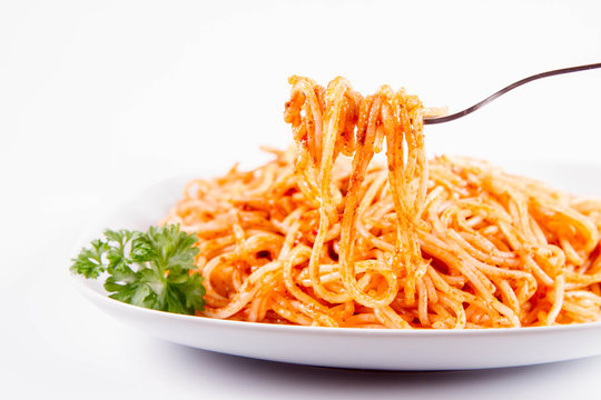 Spaghetti with pesto rosso decorated with parsley eaten with a fork on a white background