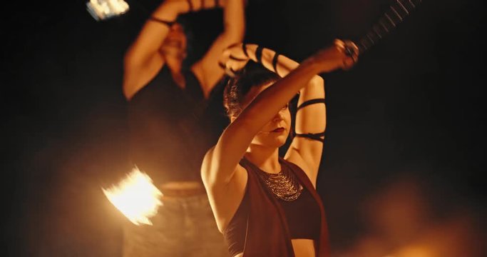 Coll fire show artists having a performance in the dark, swinging fire pieces, and looking at camera - slow motion 4k