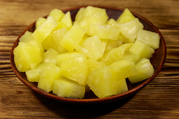 Canned pineapple pieces in ceramic plate on wooden table