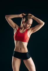 Fototapeta na wymiar awesome blond sportswoman is tiding her ponytail before the workout on the isolated black background. studio shot. preparation for a training