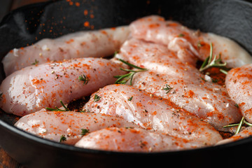Raw chicken breast mini fillets in rastic cast iron skillet, frying pan with herbs and sea salt