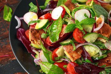Traditional fattoush salad on a plate with pita croutons, cucumber, tomato, red onion, vegetables mix and herbs