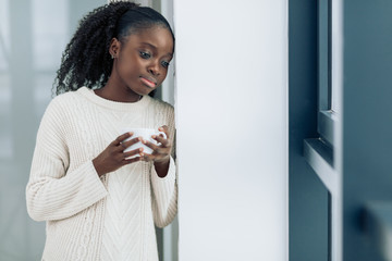 young beautiful pensive girl drinking coffee or tea and looking outside. close up photo. copy...