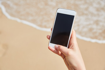 Mobile phone in female hand on the background of the beach and ocean