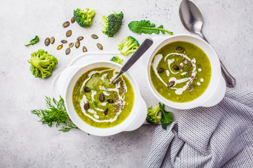 Vegan detox broccoli cream soup with coconut cream and pumpkin seeds in white bowl, top view.