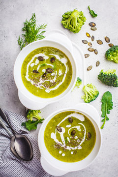Vegan detox broccoli cream soup with coconut cream and pumpkin seeds in white bowl, top view.