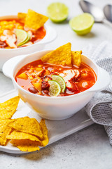 Mexican soup (Chili con carne) with beans, chicken, corn and nachos in white bowls - traditional mexican food.