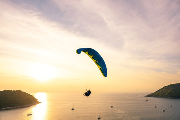 Skydiving of parachutist flying at sunset sky and sea background