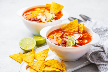 Mexican soup (Chili con carne) with beans, chicken, corn and nachos in white bowls - traditional mexican food.