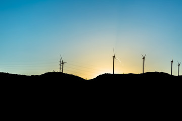 Fototapeta na wymiar Silhouette view of a wind turbines on top of mountains, sunset sky