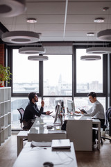Mix raced business partners planning next sales period. Indian and Chinese men in formal shirts discussing together business plan sitting opposite each other at pc computers.