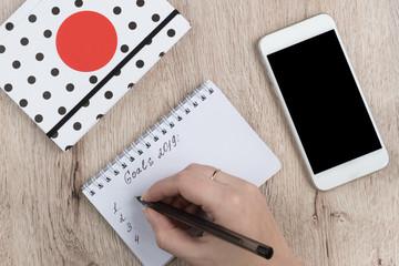 young woman hands hold opened notebook pages with black pen on  wooden table. Goals 2019 list.
