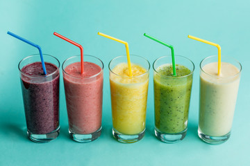 glasses with fresh delicious smoothie and straw on isolated blue background. health and body care