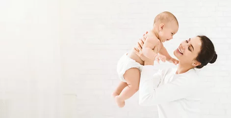 Fototapeten Young mom holding her happy baby in air © Prostock-studio