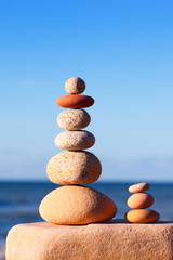 Rock zen pyramid of white and pink pebbles on a background of blue sky and sea.