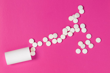 Circle pills tablets spilling out of a white plastic medicine bottle on pink background