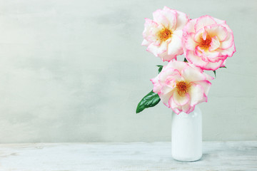 Roses in retro white vase on wood table on gray wall with copy space.