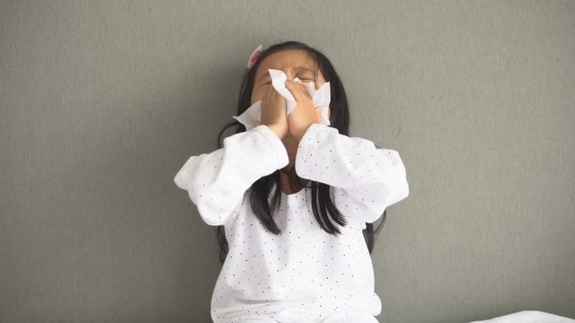 Asian child or kid girl sick with sneezing on nose and cold cough on tissue paper because weak or virus and bacteria from dust weather and kindergarten and pre school for medical background gray space