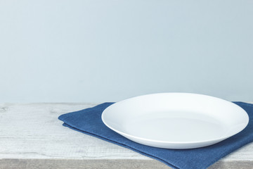 Empty plate on tablecloth on wooden table over grunge blue background