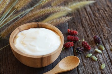 Plain organic yogurt in wooden bowl berry fruit, grain and wood spoon on wood texture background