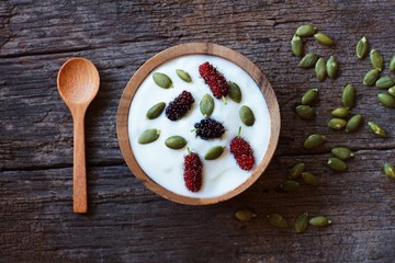 Homemade plain organic yogurt mixed with fresh berry fruit and cereal in wooden bowl and wood spoon on wood texture background