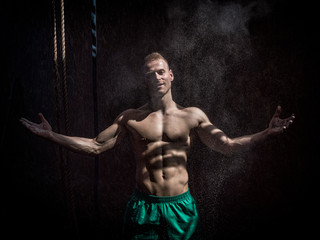 Fototapeta na wymiar Shirtless man using chalk or magnesium powder in gym, clapping hands and creating cloud
