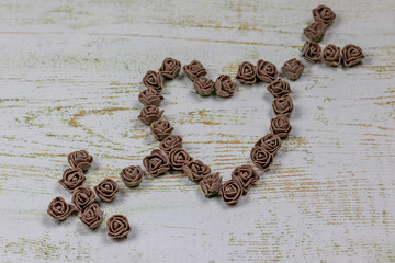 Heart pierced by an arrow made of brown roses. On wooden background, photo bokeh. Feast of love, Valentine's Day. Postcard with copy space.