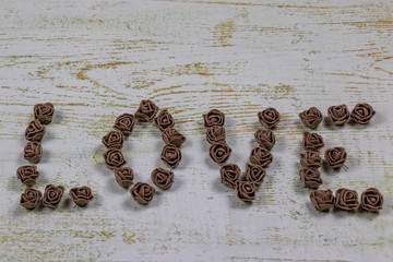 Dark brown love letters of roses on a wooden background, side view of bokeh. Text love on a wooden background in the center. Congratulations on the holiday beloved.