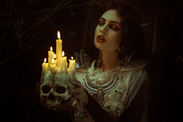 candles in skull, vampire, demonic woman dressed in white lace and silver jewelry. has fangs and thick brown hair - obrazy, fototapety, plakaty