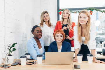 Red-haired teacher explaining new material on economics to her beautiful female students, while having lesson at cafe. People and education concept.