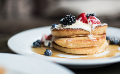 Stack of pancakes with fruit and syrup served for breakfast