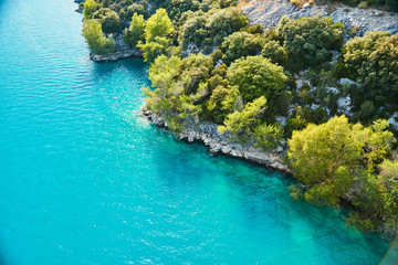 azure water of the lake and slopes of mountains on a background,  coast line, green trees, sun light