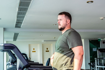Fototapeta na wymiar Sweating chubby man walking on running track, warming up on gym treadmill