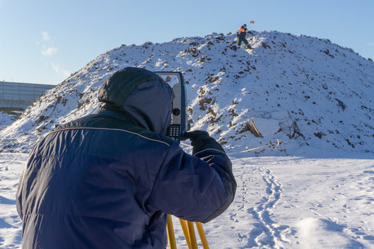 Surveyor and assistant conduct a topographical survey in the winter for cadastral work