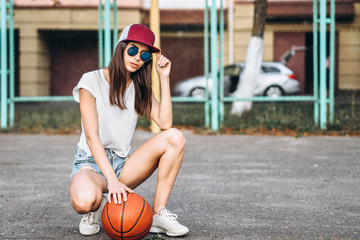 Pretty young sporty girl with basketball ball outdoor.