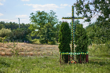 Traditional Catholic cachapel near the road in the shape of a cross with plastic artificial flowers, Biale, Poland