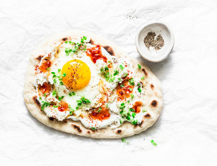 Flatbread with fried egg, yogurt, chili sauce and cheese on light background, top view