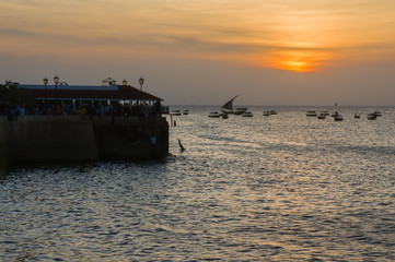 Children jump from the pier into the sea. Silhouettes at sunset. Summer travel.Stone Town, Zanzibar, Tanzania.
